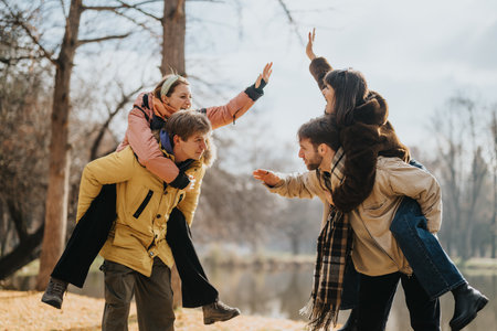 Two joyful piggybacking couples having fun together in a scenic autumn parkの写真素材