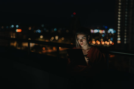 Businesswoman working late with tablet on rooftop with city lightsの写真素材