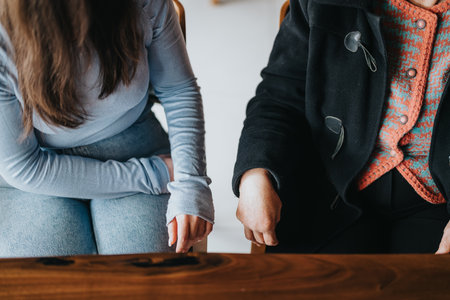 Close-up of Two Individuals Sharing a Conversation at a Wooden Tableの写真素材