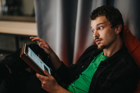 Young man engaged with a digital tablet while displaying a thoughtful expressionの写真素材