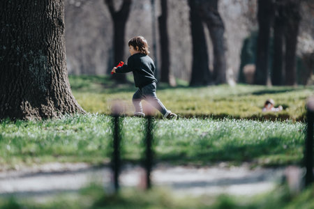 Child running in a sunlit park with vibrant grass and trees, expressing joy and interaction with nature.の写真素材