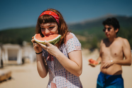Friends enjoying a summer day eating watermelon at the lakeside beachの写真素材