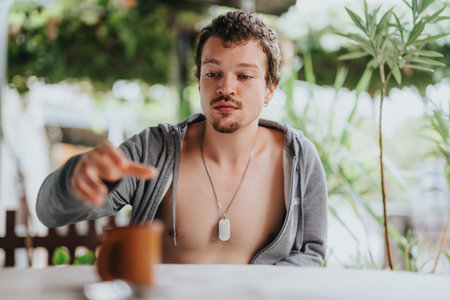 Young man in casual attire reaching for a coffee cup at a relaxed outdoor setting