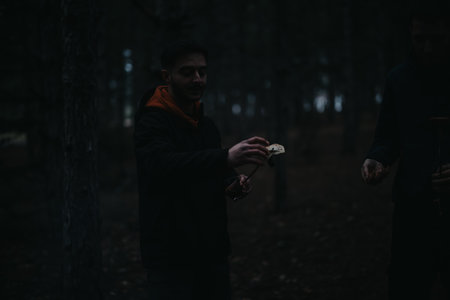 Outdoor gathering in a forest setting during low light conditions, portraying camaraderie around cooking.の写真素材