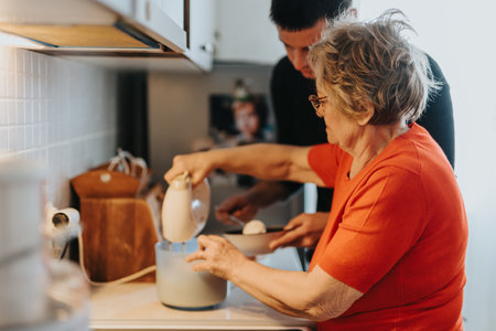 Elderly Woman Baking in Kitchen with Family Member Providing Assistanceの写真素材