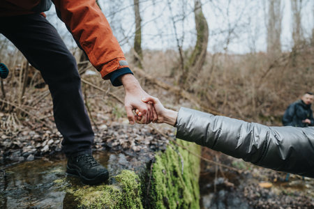 Two people assisting each other while crossing a forest stream in a wintery natural setting