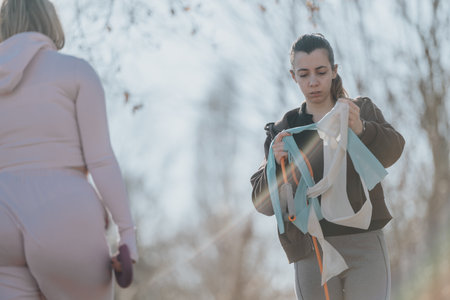 Two women engaging in outdoor fitness activities with resistance bands on a sunny day in the parkの写真素材