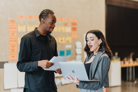 Two people discussing work while using a laptop in a modern office settingの写真素材