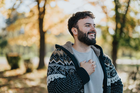 Joyful man in a cozy sweater enjoying a beautiful autumn day outdoorsの写真素材