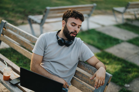 Young man taking a nap outdoors on a park bench with headphonesの写真素材