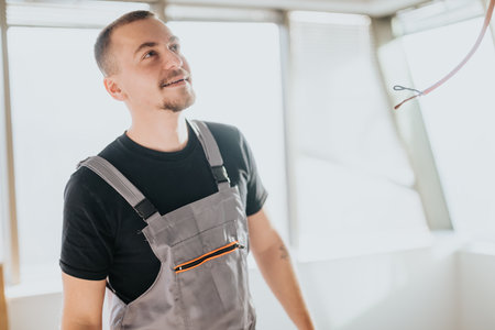 Smiling electrician in overalls planning work in a sunny room interior