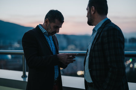 Business professionals sharing an evening conversation on a stylish rooftopの写真素材