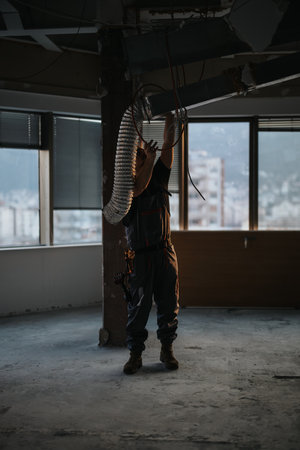 Construction worker adjusting ventilation tubing in an unfinished building during renovationの写真素材
