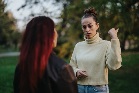 Two women conversing in a park during autumn afternoonの写真素材