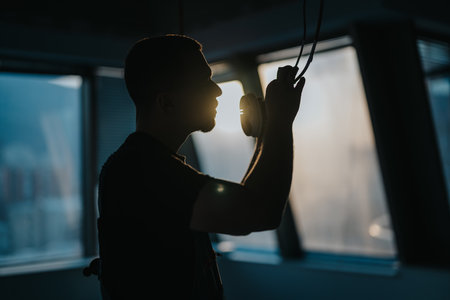 Silhouetted man adjusting headphones in a sunlit room, emphasizing serenity and modern workspaceの写真素材