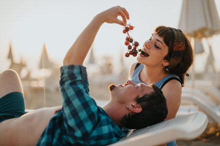 Couple enjoying a relaxing beach day sharing fresh grapesの写真素材