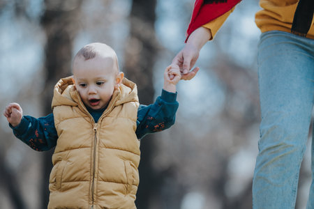 Young child learning to walk with parental assistance outdoors on a sunny day