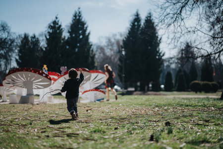 Young child enthusiastically playing outdoors near decorative mushroom figures on a sunny day in a scenic parkの写真素材