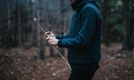 Person carving wood with a knife in a forest setting during a cold season