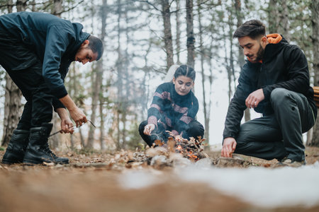 Three Friends Setting Up a Campfire in a Forest During Wintertimeの写真素材