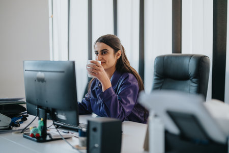 Businesswoman enjoying a coffee while working on her computer in the officeの写真素材