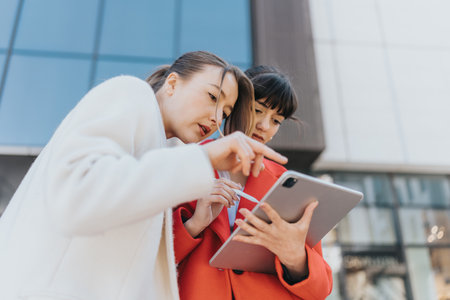 Two businesswomen collaborating with a digital tablet outdoors in a modern urban environmentの写真素材
