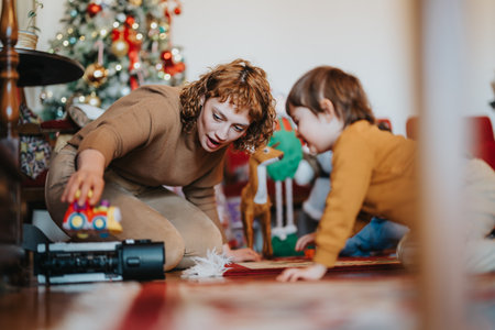 Mother and child playing together by a Christmas tree during a festive holiday moment.の写真素材