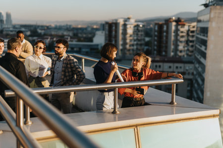 A diverse group of business coworkers stands on a rooftop balcony, engaged in lively discussions.の写真素材