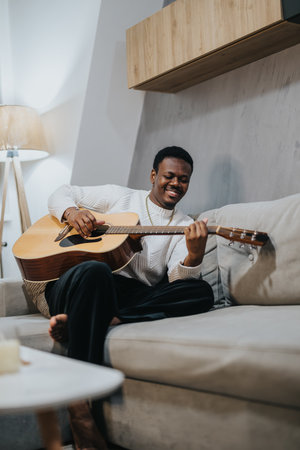 Man relaxing on a sofa playing an acoustic guitar in a warm modern interior settingの写真素材