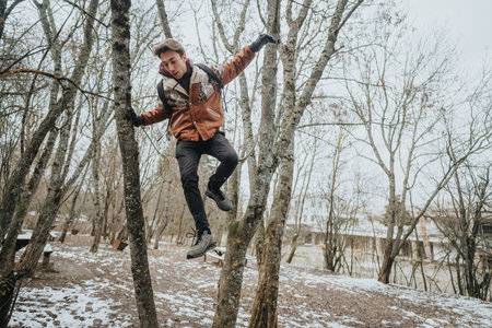 Young man climbing trees in a snowy forest enjoying an adventurous winter day outdoorsの写真素材