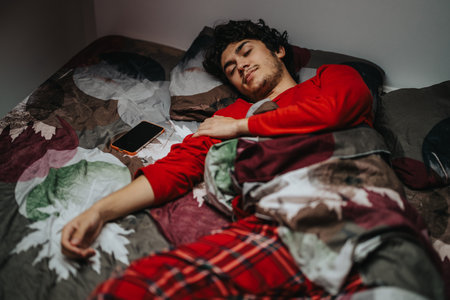 Young man peacefully sleeping in cozy bed with smart phone nearby