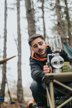 Man preparing coffee at a camping table in a forest setting, enjoying a casual winter picnicの写真素材