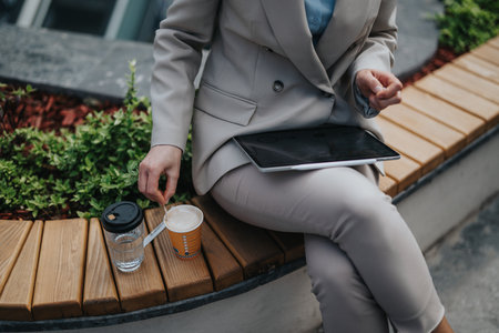 Businesswoman enjoying a coffee break outdoors with a tablet and beverageの写真素材