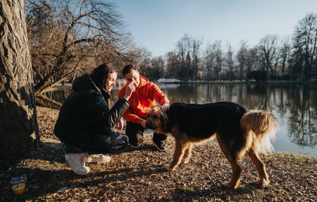 Couple interacting with dog during a park visit by the pondの写真素材