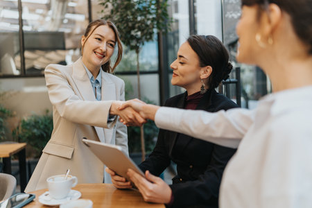 Two businesswomen engaging in a handshake agreement during a professional meeting in a cafeの写真素材