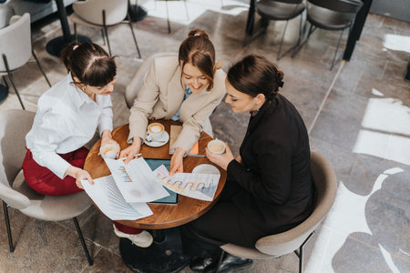 Three businesswomen discussing charts and reports over coffee at a modern cafe table.の写真素材