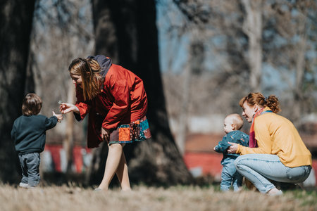 Two women interacting with young children outdoors during a playful and joyful gathering in a sunny...