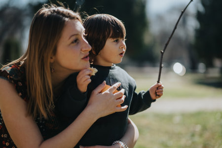 Mother and child bonding outdoors in a park holding a stick on a sunny dayの写真素材