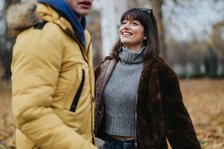 Smiling young individuals outside in a park, wearing warm jackets during fallの写真素材