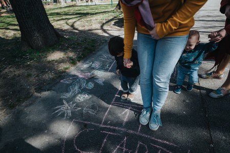 Children Drawing with Chalk on Pavement Under Parental Supervisionの写真素材