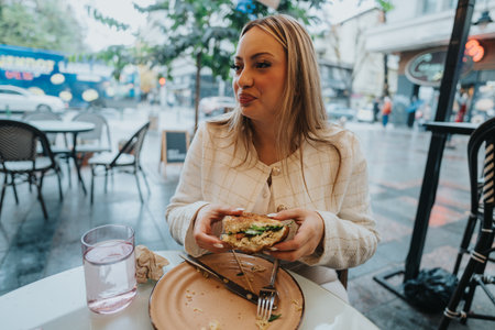 Woman enjoying a sandwich at an outdoor cafe on a rainy dayの写真素材