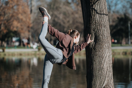 Person stretching outdoors by a tree in a green park near a lakeの写真素材