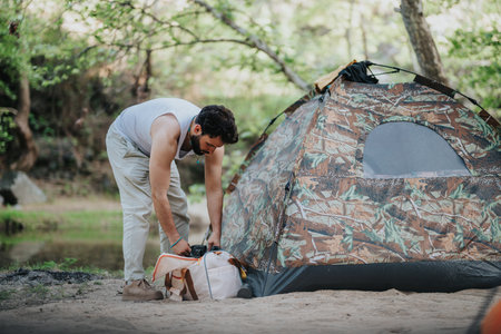 Man setting up a tent near a river in a natural settingの写真素材