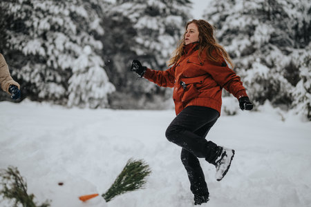 Woman Enjoying Winter Outdoors While Playing in a Snowball Fight Among Snow-Covered Treesの写真素材
