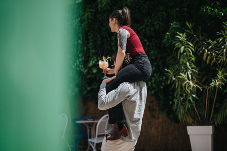 Woman sitting on friends shoulders enjoying a cocktail in an outdoor settingの写真素材