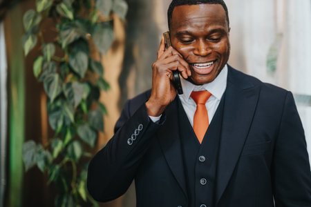 Professional businessman in a suit conversing on a mobile phone with an office plant background.の写真素材