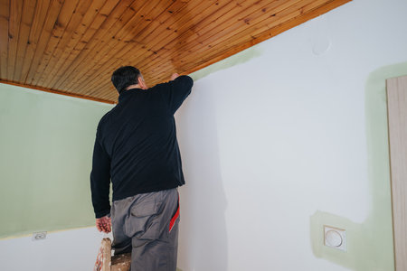 Worker Painting Room with Brush on Wooden Ceiling and White Wallの写真素材