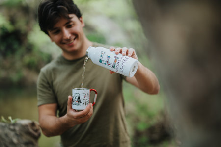 Smiling camper pouring water into a cup outdoors in a forest settingの写真素材
