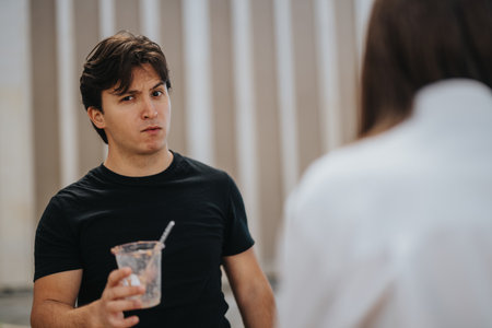 Man holding drink cup making confused gesture while engaging in casual conversationの写真素材