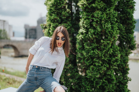 Young woman posing playfully outdoors in casual outfit with vibrant greeneryの写真素材